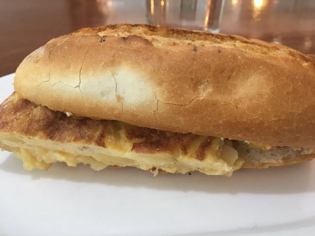 Bocadillo de tortilla de patata partido, visto de lado en un plato blanco